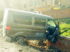 面包车冲出道路 卡在墙顶被架悬空